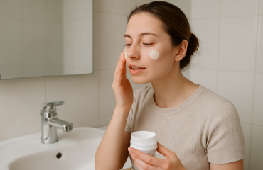 personne appliquant crème sur visage au lavabo